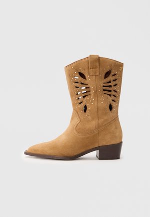 Stivale da cowboy in suede tan con design a ritaglio e borchie decorative. Punta affusolata e tacco impilato. Presenta una linguetta per un facile inserimento.