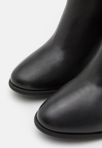 Bottines noires en cuir lisse, dotées d'un bout pointu et d'une semelle fine et texturée. Le design est épuré avec une finition minimaliste.