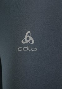 Donkergrijze sportleggingen met een textuurafwerking, voorzien van een reflecterend logo in een contrasterende kleur nabij de onderste linkerkant.