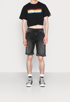 Černé zkrácené tričko s viacbarevným logem, spárované se šedými džínovými šortkami s ohrnutými lemy a černými vysokými teniskami.