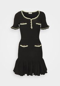 Schwarzes geripptes Kleid mit kurzen Ärmeln, rüschigen Kanten, kontrastierendem hellgrünem Besatz, zwei Brusttaschen und einem ausgestellt geschnittenen Rock.