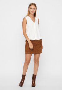 Haut sans manches blanc avec décolleté en V, associé à une mini-jupe en cuir suédé marron. Le modèle porte des bottines à talons marron. Textures lisses, design décontracté.