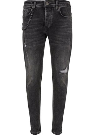 Čierne džínsy s priliehavým strihom, ktoré majú opotrebované detaily a reťaz ako akcent na prednej kapse. Hladká textúra s vyblednutým povrchom.