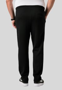 Los pantalones de chándal negros presentan un ajuste relajado, cinturilla elástica y un bolsillo trasero. El material parece suave con un acabado ligeramente texturizado.