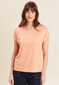 Perzikkleurige T-shirt met korte mouwen, gemaakt van lichte stof met een subtiele glans. Beschikt over een ronde halslijn en opgerolde mouwomslagen.