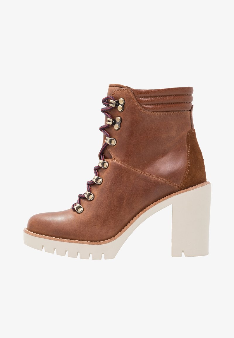 Bottine en cuir marron avec un talon carré, avant lacé avec des œillets métalliques et des lacets violets contrastants. Accents texturés sur le talon.