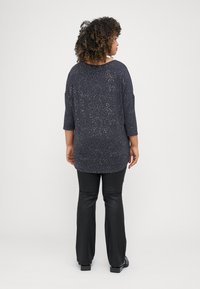 Sötét tengerészkék, háromnegyedes ujjú felső, foltokkal mintázva, fekete nadrággal és lapos cipővel párosítva, hátulról nézve.