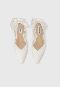 Τα λευκά σατέν παπούτσια με μυτερή μύτη διαθέτουν σχέδιο με κοπή στα πλαϊνά, μεγάλους λευκούς φιόγκους στα λουράκια των αστραγάλων και ανοιχτό καφέ εσωτερική σόλα.