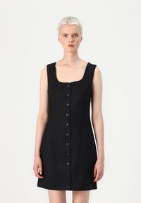 Zwarte mouwloze jurk met een vierkante halslijn en een knoopsluiting aan de voorkant, met een getailleerde bodice en een uitlopende rok. Soepele textuur, minimalistisch ontwerp.