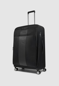 Maleta negra con un exterior de tela texturizada, un detalle en cuero liso, cuatro ruedas y un asa retráctil para facilitar su maniobrabilidad.