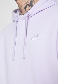Lila sweatshirt med huva, har en kanguruficka framtill och en vit broderad Nike-logotyp på vänster bröst. Justerbara dragsnören.