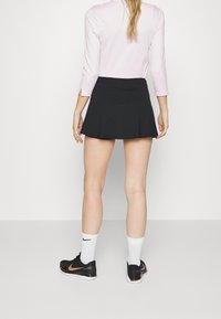 Svart skorts med en utsvängd design, i kombination med en ljusrosa långärmad topp. Svarta och orange sneakers med vita strumpor slår an tonen i stilen.