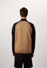 Ruskea ja musta pitkähihainen collegepaita, jossa on korkea kaulus ja raglan-hihat, sileä pinta ja istuva malli.