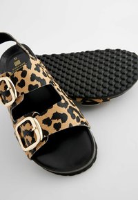 Sandalice na klizanje s uzorkom leoparda, s dva zlatna kopčanja, crna unutrašnjost i rebrasti gumeni potplat s heksagonalnim uzorkom.