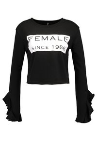 Svart kort sweatshirt med långa, volangärmar. Har vit text som säger "FEMALE SINCE 1986" på framsidan i fet stil.