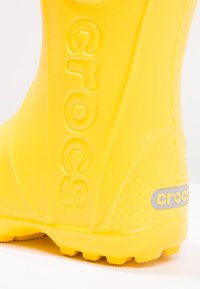 Żółte kalosze Crocs z materiału teksturowego, wypukłym logo oraz wzorzystą podeszwą z kolcami dla lepszej przyczepności. Lekka i wodoodporna konstrukcja.