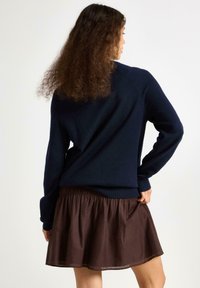 Marinblå stickad tröja med långa ärmar, med en avslappnad passform och textilstruktur. Parat med en brun, plisserad minikjol.