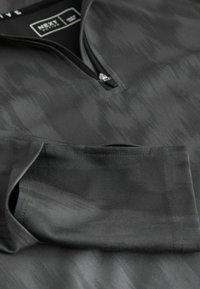 Schwarzer Half-Zip-Pullover mit strukturiertem Muster aus glattem Stoff. Besitzt lange Ärmel und subtile Nahtdetails.