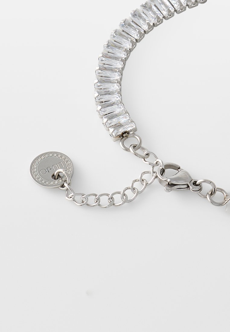 Silberne Kettenarmband-Sektion mit rechteckigen klaren Steinen, einem Karabinerhaken und einer verstellbaren Kette, die in einem runden Markenanhänger endet.