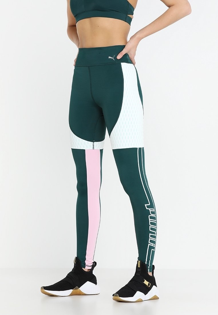 Leggings verdi con accenti rosa e bianchi, vita alta, elementi in tessuto a rete e logo grafico audace sul lato. Abbinati a scarpe sportive nere.