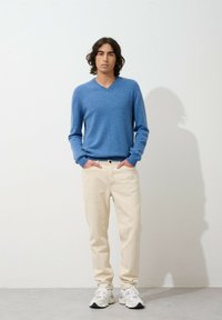 Lichtblauw, v-hals trui gemaakt van zachte stof; gecombineerd met crèmekleurige jeans en witte sneakers met grijze accenten; casual fit.