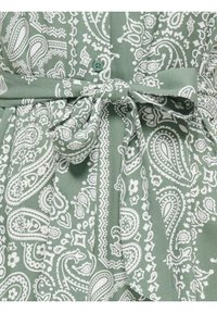 Tissu vert à imprimé paisley blanc, détail avec boutons et ceinture assortie nouée en nœud à la taille.
