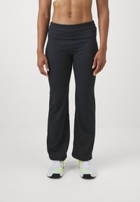 Black fitness pants with a wide waistband, sleek design, and a flowing silhouette, paired with gray and neon green athletic shoes.