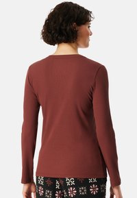 Langwerpige, bordeauxrode shirt met een geribbelde textuur, ronde halslijn en een regular fit, gecombineerd met zwarte broek met patronen en florale details.