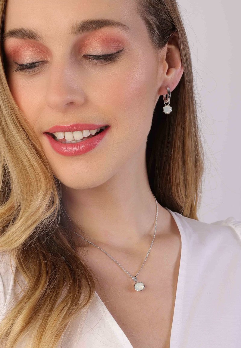 Boucles d'oreilles en argent avec une perle ronde suspendue et un collier en argent avec un pendentif présentant une pierre irisée sur une fine chaîne.
