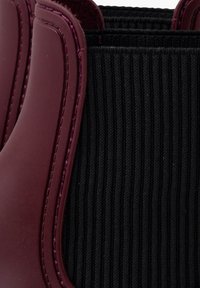 Bottes de cheville en caoutchouc bordeaux avec des panneaux latéraux en élastique noir ; elles présentent une texture côtelée et un détail de couture contrasté.