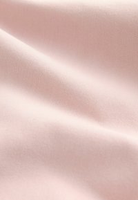 Tissu rose pâle doux avec une texture lisse, légèrement pliée et un motif de tissage fin visible en gros plan.