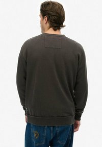 Ciemnoszara bluza z długimi rękawami, okrągłym dekoltem i teksturowaną tkaniną. Posiada małą prostokątną naszywkę na plecach oraz ściągacze na rękawach.