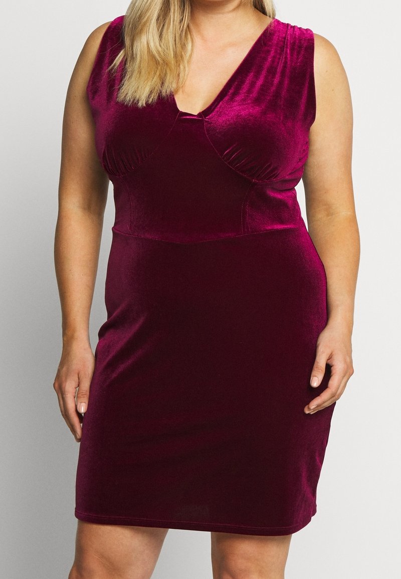 Robe sans manches en velours magenta profond avec un détail froncé au niveau de la poitrine portée par une personne aux cheveux blonds, visible du cou jusqu'au milieu de la cuisse.