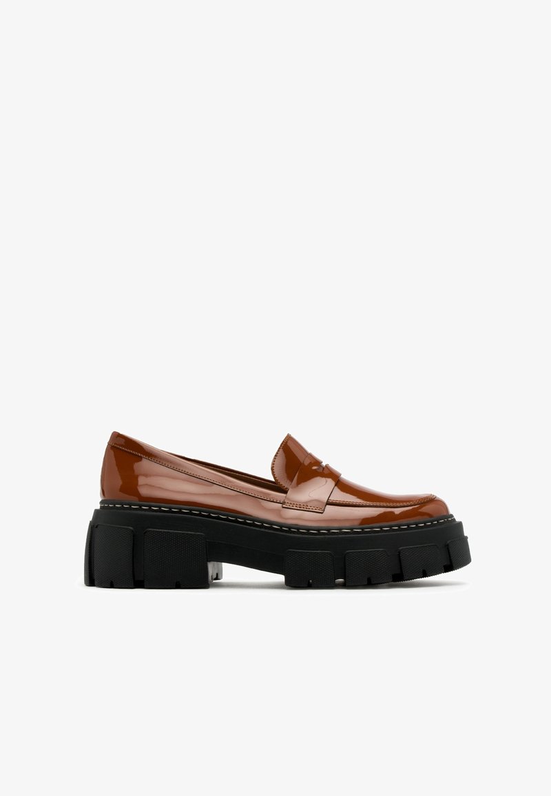 Mocasines de charol marrón con suela de plataforma negra gruesa y costuras blancas en contraste. Punta redondeada y detalle clásico de tira de penique.