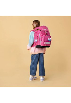 Child wearing a large pink backpack with star and unicorn designs, dressed in blue striped pants, pastel sweater, and lavender sneakers, standing sideways.
