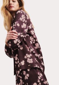 Lila, mit Blumen bedruckter Stoffset, bestehend aus einem Oberteil mit langen Ärmeln und einem Saumakzent, kombiniert mit passenden Hosen, glatt in der Textur.