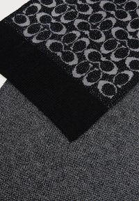 Cachecol de malha preto com um padrão texturizado em cinza, apresentando círculos interligados. A metade inferior é feita de um tecido cinza texturizado sólido.