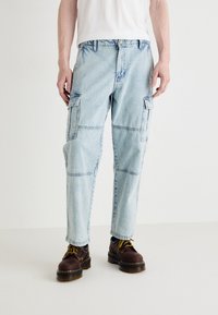 Lyseblå denim cargo bukser med flere lommer, en avslappet passform og kontrasterende sømmer, kombinert med mørkebrun snøresko.