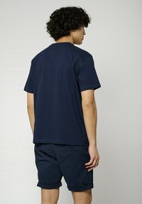 T-shirt en coton bleu marine à manches courtes, col rond et coupe décontractée, associé à un short bleu marine avec des revers et des poches latérales.