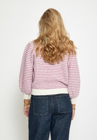 Kofta i rosa och vit randig mönster med puffärmar och ribbad vit nederkant, matchad med mörk denimbyxor.