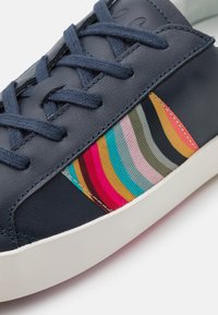 Baskets en cuir bleu marine avec un panneau rayé multicolore aux nuances de rose, bleu, vert et jaune. Semelle en caoutchouc blanche et lacets texturés.