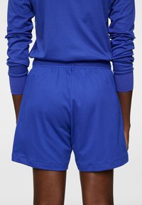 Sinisiä urheiluhousuja, jotka on valmistettu pehmeästä kankaasta, elastisella vyötärönauhalla ja minimaalisen ompelun yksityiskohdilla, suunniteltu mukavuuteen ja joustavuuteen.