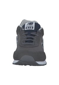 Graue Sportschuhe mit einem strukturierten Obermaterial, Schnürung in der Mitte und einer weißen Mittelsohle. Mit einem Logo und Modellnummer auf der Zunge.