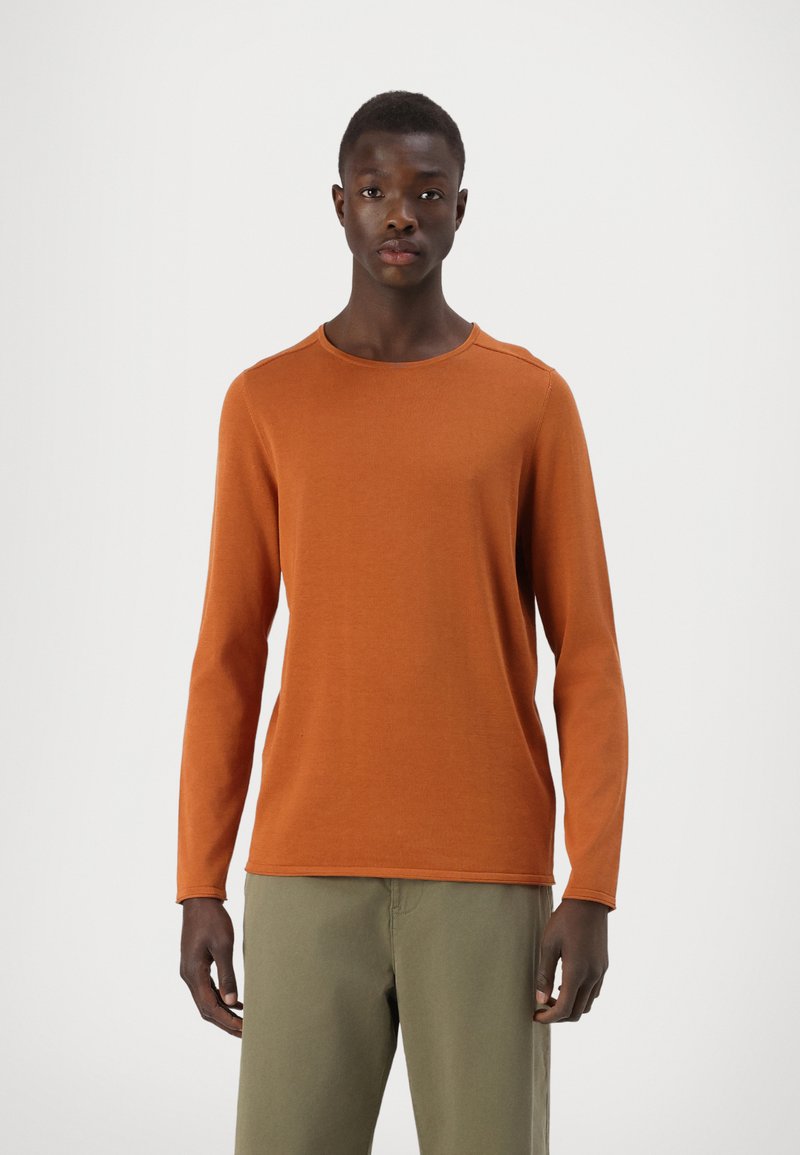 Langarmshirt mit Rundhalsausschnitt aus burnt orange Strickstoff. Verfügt über eine glatte Textur und einen Standard-Schnitt, kombiniert mit hellgrünen Hosen.