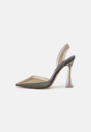 Kärkikärkinen korkeakorkoinen kenkä, jossa on läpikuultava beige päällinen ja kirkas levenevä korko, jossa on slingback-nauha valkoisella taustalla.