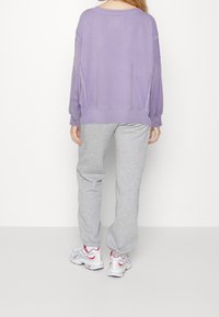 Felpa oversized viola, pantaloni della tuta grigi e sneakers bianche con accenti rossi. Presenta una vestibilità comoda e texture morbide.