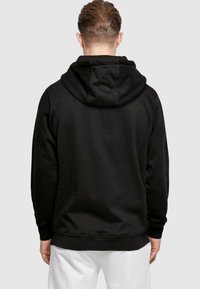 Sort hoodie med hætte, der har en glat tekstur og ribbede manchetter og kant. Designet med en afslappet, løs pasform.