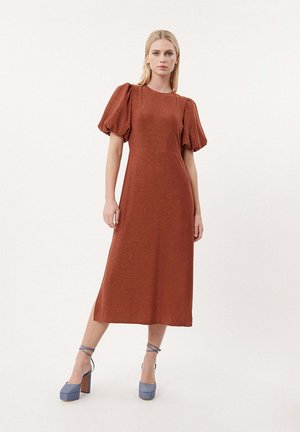 Roodbruine midi-jurk met pofmouwen, gemaakt van textiel met structuur. Gepaarde met blauwe platformhakken met enkelriempjes.