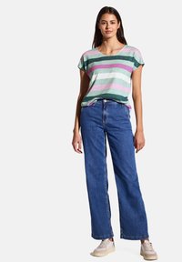 Pruhované tričko s krátkým rukávem v zelené, růžové a modré barvě spárované s volnými modrými džínami. Tento outfit má uvolněný střih a ležérní tenisky.