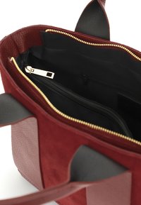 Bordeaux tote taske med en glat læderbund og suede-detaljer. Indvendig har den en guldlynlås lomme og sort stofforing.
